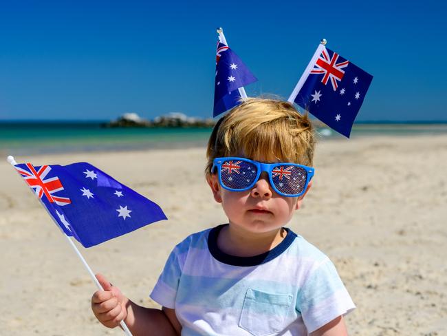 Cute smiling kid with Australian flags sitting on the sand at the beach on Australia Day