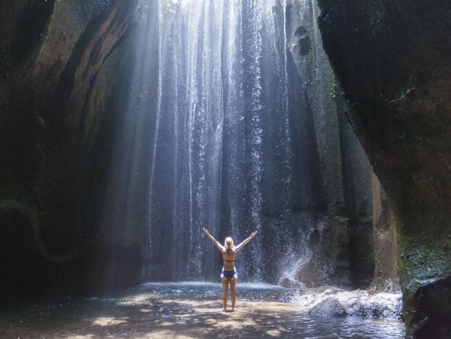 ESCAPE: Happy woman traveler with raised arms enjoying life at a beautiful rainforest waterfall in Bali Picture: Istock