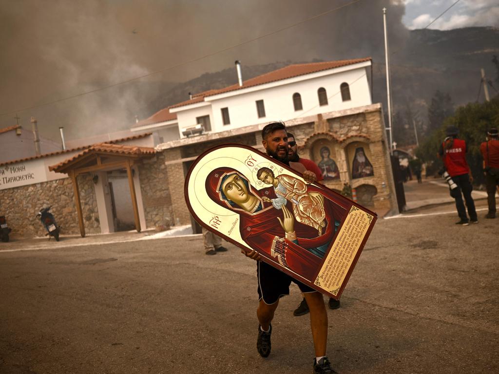 A volunteer carries an icon from a burning monastery as a wildfire spreads in Acharnes, north of Athens. Picture: Angelos Tzortzinis / AFP