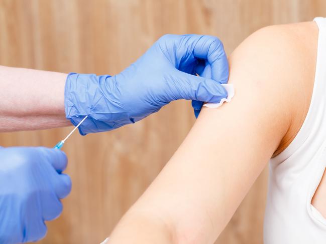 Medical assistant preparing an intramuscular injection of a vaccine disinfecting arm of young woman in a clinic