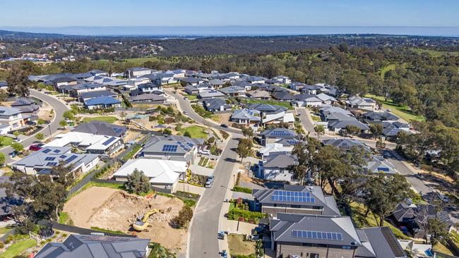 Aerial view of houses and streets in new wealthy suburb in Adelaide foothills with construction in foreground and coastline in background: large houses, landscaped gardens, rooftop solar systems,