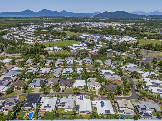Developing Queensland - Aerial, wide angle view , looking down on established Cairns  suburb, reserve green space, Coral Sea & ranges in distance. Single level living with dwellings close together on housing blocks. Most houses with solar panels installed. Tropical climate, tropical trees, landscaped gardens.
