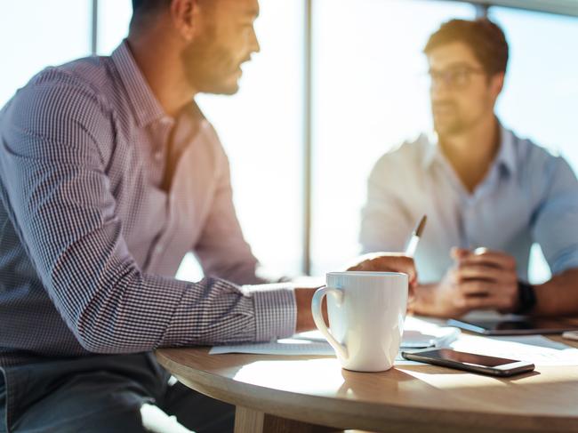 Business executives discussing work at office. Closeup of coffee cup with blurred image of two businessmen sitting on table. Picture: istock