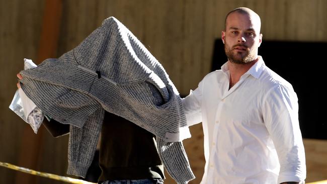 Sarah Budge, girlfriend of Kings Cross identity John Ibrahim, hides under a jumper as her brother Jack Budge escorts her from Sydney Police Centre. Picture: AAP/Dan Himbrechts