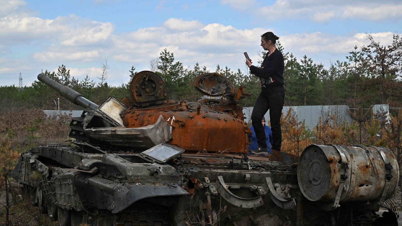 A woman takes a photograph as she stands on a destroyed Russian tank in Dmytrivka village, Kyiv. Photo by Sergei SUPINSKY / AFP