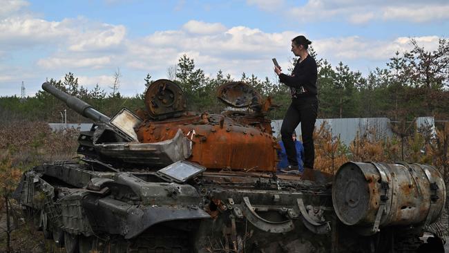 A woman takes a photograph as she stands on a destroyed Russian tank in Dmytrivka village, Kyiv. Photo by Sergei SUPINSKY / AFP