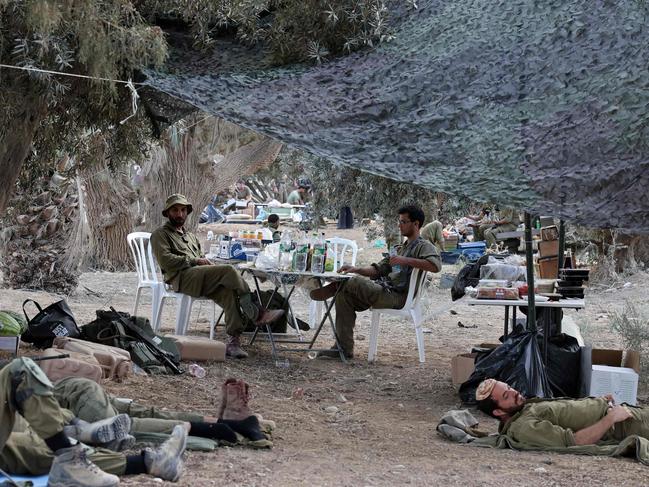 Israeli soldiers holding a position rest in a field near the kibbutz Beeri in southern Israel on October 14, 2023, close to the spot where 270 revellers were gunned down or burnt in their cars by Hamas gunmen at the Supernova music festival in the Negev desert on October 7. Hamas launched a large-scale attack on Israel on October 7 which killed at least 1300 people, sparking a retaliatory bombing campaign that has killed more than 1900 in the Gaza Strip ahead of a potential Israeli ground invasion of the territory. (Photo by Thomas COEX / AFP)