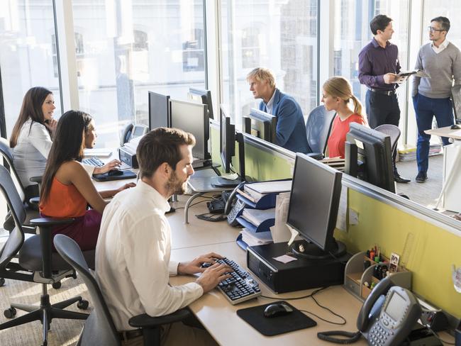 A photo of multi-ethnic business people working together. Professionals are using computers and discussing. Desks are located near windows, in brightly lit modern office.