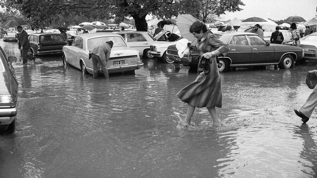 A woman holds her shoes as she makes her way through a flooded carpark in 1976.