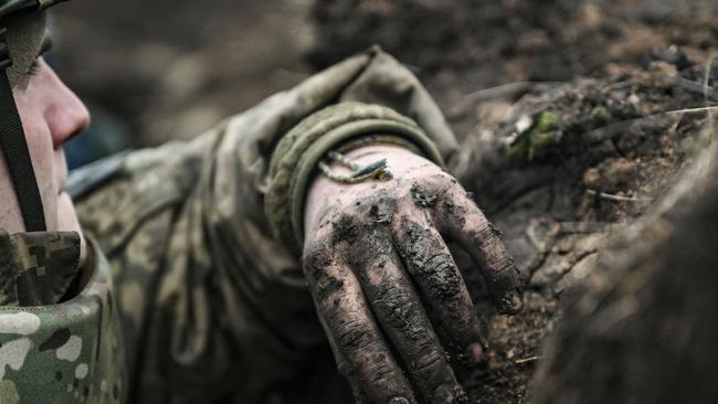 TOPSHOT - A Ukrainian serviceman takes cover in a trench near Bakhmut in the Donbas region on March 8, 2023. - After a cold and snowy winter, the arrival of spring with rain and milder temperatures has brought back the mud on the Donbas battle fields. Trenches that have become baths where soldiers wade through and trucks, armoured cars and sometimes tanks destroyed after getting stuck in mud. (Photo by Aris Messinis / AFP)