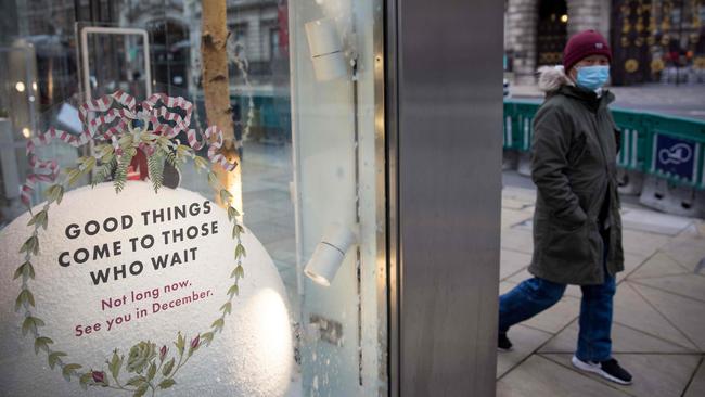 A pedestrian wearing a face mask walks past a notice reading “Good things come to those who wait” as they pass a Christmas-themed window display in London. Picture: AFP