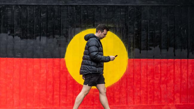 VOICEREF23. A Pedestrian walks past a gate painted in the Aboriginal flag on the day of the referendum in South Yarra, VIC. Melbourne. Picture: Jake Nowakowski