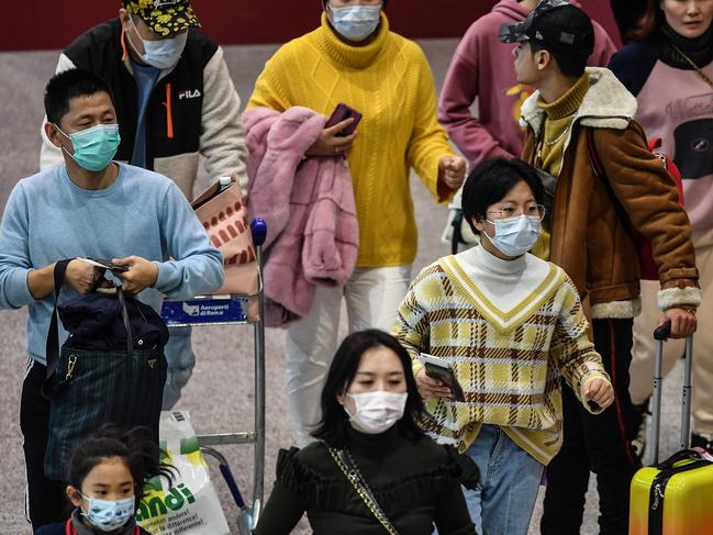 Passengers wearing respiratory masks walk across a terminal towards the check in counter on January 31, 2020 at Rome's Fiumicino airport, as a number of airlines halted or reduced flights to China while the country struggles to contain the spread of the deadly novel coronavirus. - The Italian government said on January 30, 2020 it was suspending all flights between Italy and China, adding it was the first EU government to do so. China has advised its citizens to postpone trips abroad and cancelled overseas group tours, while several countries have urged their citizens to avoid travel to China. (Photo by Tiziana FABI / AFP)