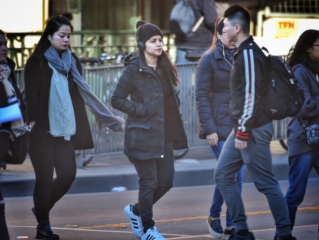 Pedestrians wearing headphones crossing Flinders St. Picture: Tony Gough