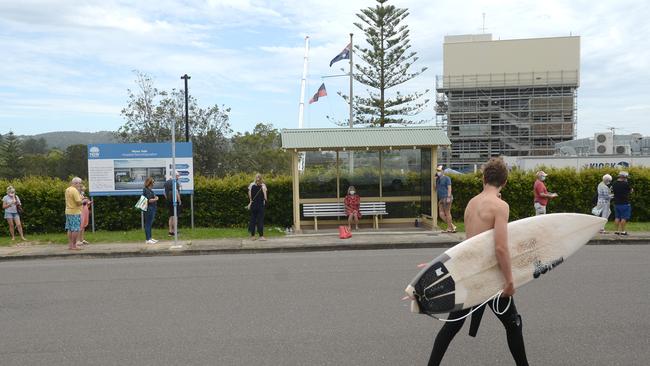 A surfer looks on as residents line up at Mona Vale Hospital for a COVID-19 test on Thursday. Picture: NCA NewsWire/Jeremy Piper