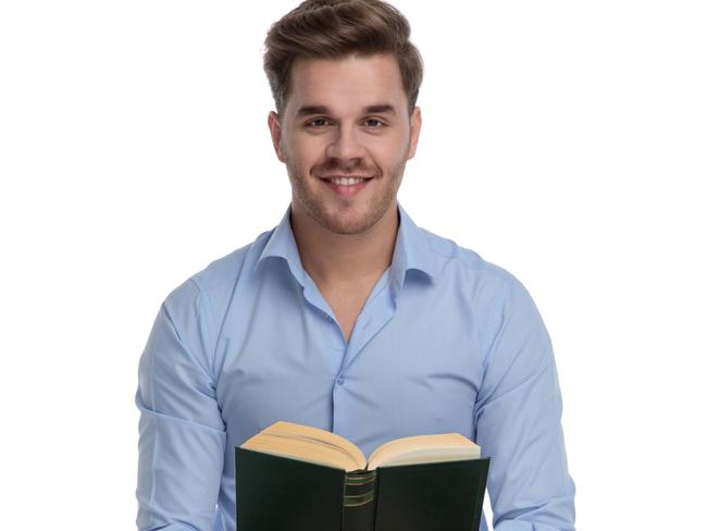 CAREERS: Positive casual man reading book and smiling while sitting on a chair on white studio background