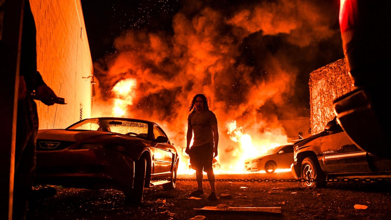 A man tries to toe away a car in a safe zone as the other car catches fire in a local parking garage on May 29, 2020 in Minneapolis, Minnesota. Picture: AFP