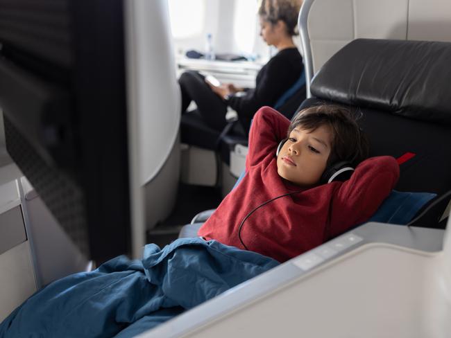 Latin American boy traveling by plane in business class and watching a movie using headphones