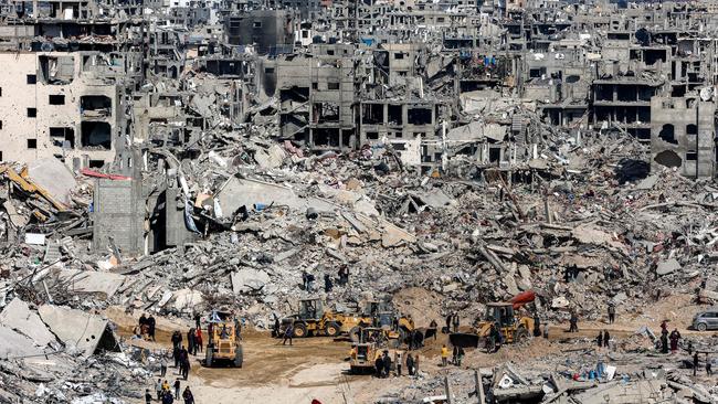 Palestinians walk near bulldozers past the rubble of collapsed buildings at the Jabalia camp for Palestinian refugees in the northern Gaza Strip. Picture: AFP.