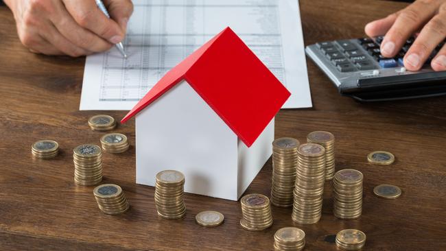 Cropped image of businessman calculating tax by model house and stacks of coins on table