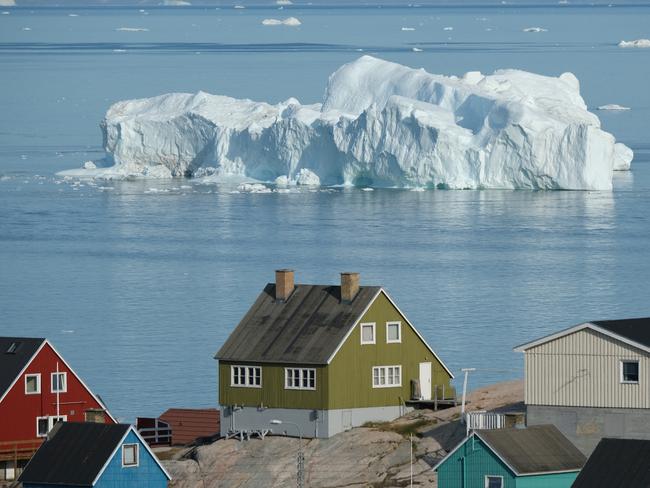 ILULISSAT, GREENLAND - JULY 30: An iceberg floats in Disko Bay behind houses during unseasonably warm weather on July 30, 2019 in Ilulissat, Greenland. The Sahara heat wave that recently sent temperatures to record levels in parts of Europe is arriving in Greenland. Climate change is having a profound effect in Greenland, where over the last several decades summers have become longer and the rate that glaciers and the Greenland ice cap are retreating has accelerated.   (Photo by Sean Gallup/Getty Images) *** BESTPIX ***