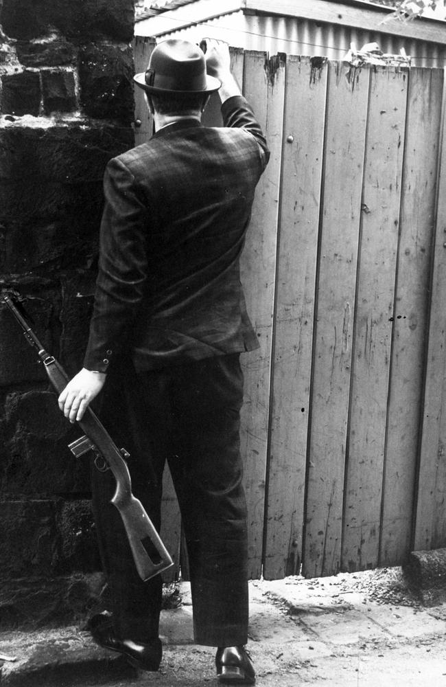 Homicide squad detective armed with a rifle outside the back fence of a Melbourne house after sighting of escapees Ryan and Walker.