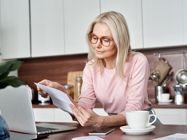 SENIOR/PENSIONER/MATURE/ELDERLY/OVER 65/GRANDPARENT/RETIREE/SUPERANNUATION. Picture: istock Middle aged older woman housewife reading paper letter or bill sitting in kitchen at home office, checking financial taxes fees, reviewing bank account loan rates information, medical insurance cost.