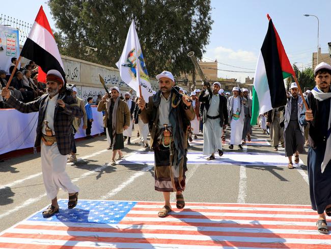 Armed Yemeni men step over a US and an Israeli flag painted on the asphalt in the Houthi-run capital Sanaa, during a march in support of the Palestinians. Picture: AFP