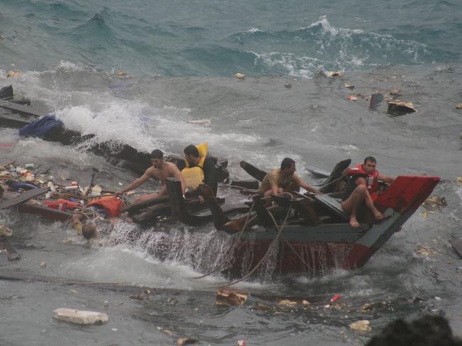 Credit: Amy Rossbach. Copyright: News Limited. Assylum seekers cling to what remains of their wooden fishing boat after it broke apart when it crashed onto cliffs while trying to land at Christmas Island, with 42 survivors pulled from the water and at least 28 were drowned. 384.jpg (DO NOT REMOVE FILENAME)