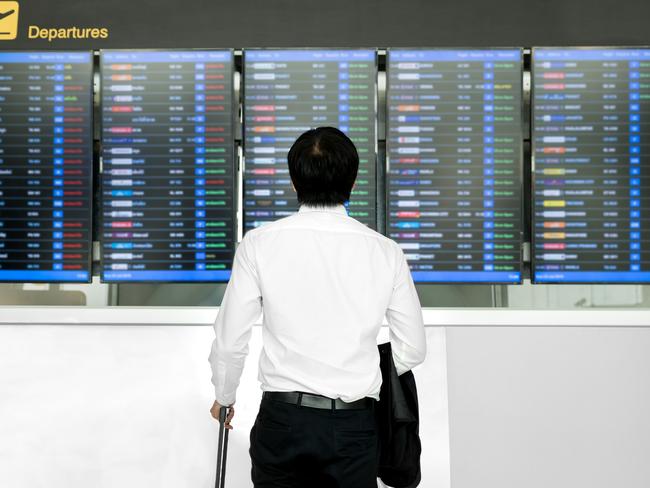 Business travel concept - Asian young business man with luggage waiting for travel in airport near flight timetable.