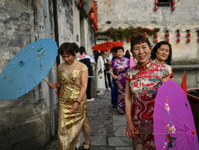 TOPSHOT - Women wearing traditional costumes are seen next to the Hongcun Wangshi ancestral temple in Hongcun village, in eastern China's Anhui province, on May 12, 2024. The ancient village, located in Yi County in Huangshan City, was added to the UNESCO World Heritage Site list in the year 2000 and is known for its scenic lake views and traditional architecture. (Photo by HECTOR RETAMAL / AFP)