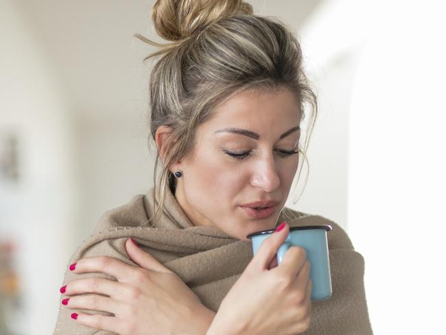 Home Expert Reducing asthma allergy Triggers. Beautiful middle-aged woman drinks tea from a glass in a cold living room dressed in a cotton becouse of cold winter. A sick girl drinks from a blue cup in the living room.