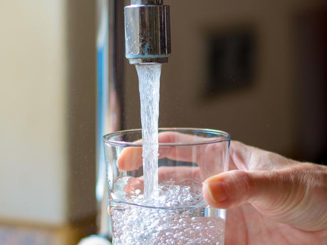 Woman filling a glass of water from a stainless steel or chrome tap or faucet, close up on her hand and the glass with running water and air bubbles