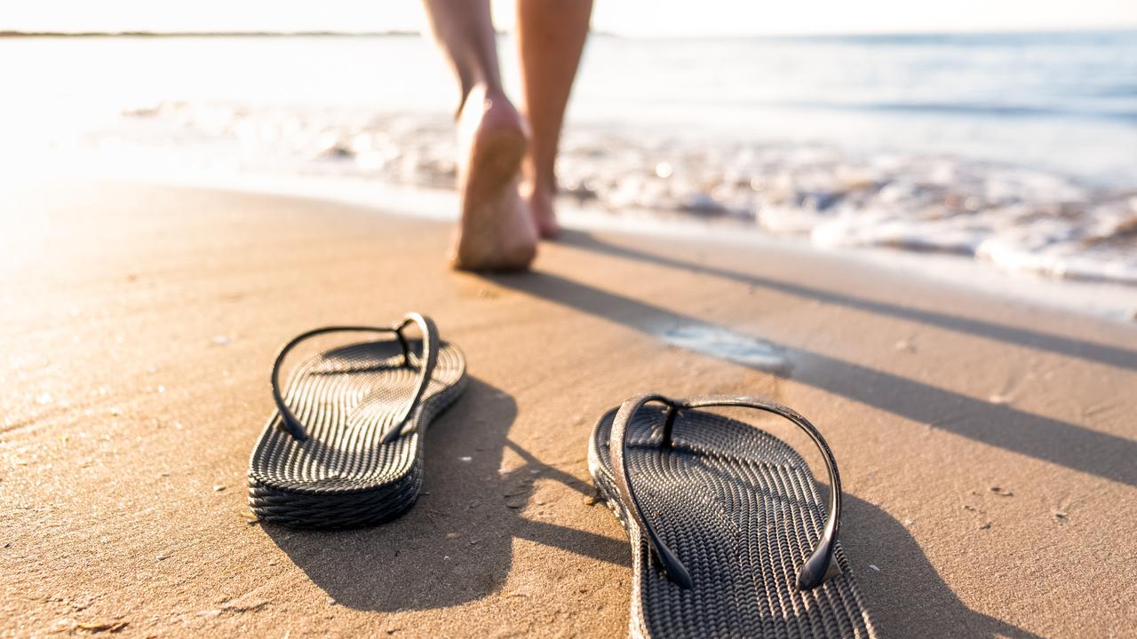 Woman's legs move away from their sandals towards the sea water on a beach