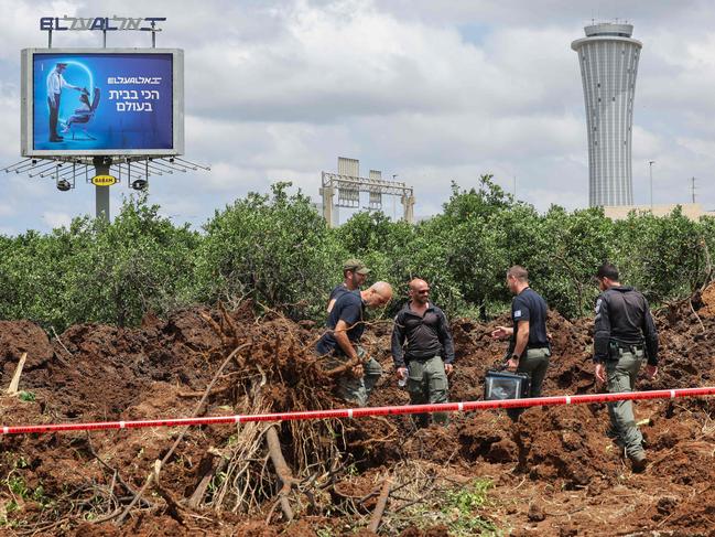 TOPSHOT - Members of Israeli security services inspect a crater near a road outside Israel's Ben Gurion airport after a missile launched from Yemen struck the area on May 4, 2025. A missile launched from Yemen struck near Israel's main international airport on May 4, Israeli authorities said, an attack that briefly halted air traffic and triggered threats of retaliation. (Photo by Jack GUEZ / AFP)