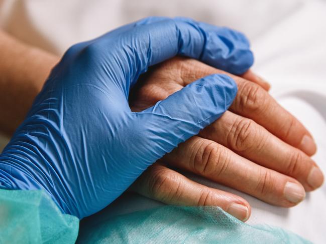 Close up of a doctor hand with blue glove giving support and love to a patient at hospital. Coronavirus pandemic concept.