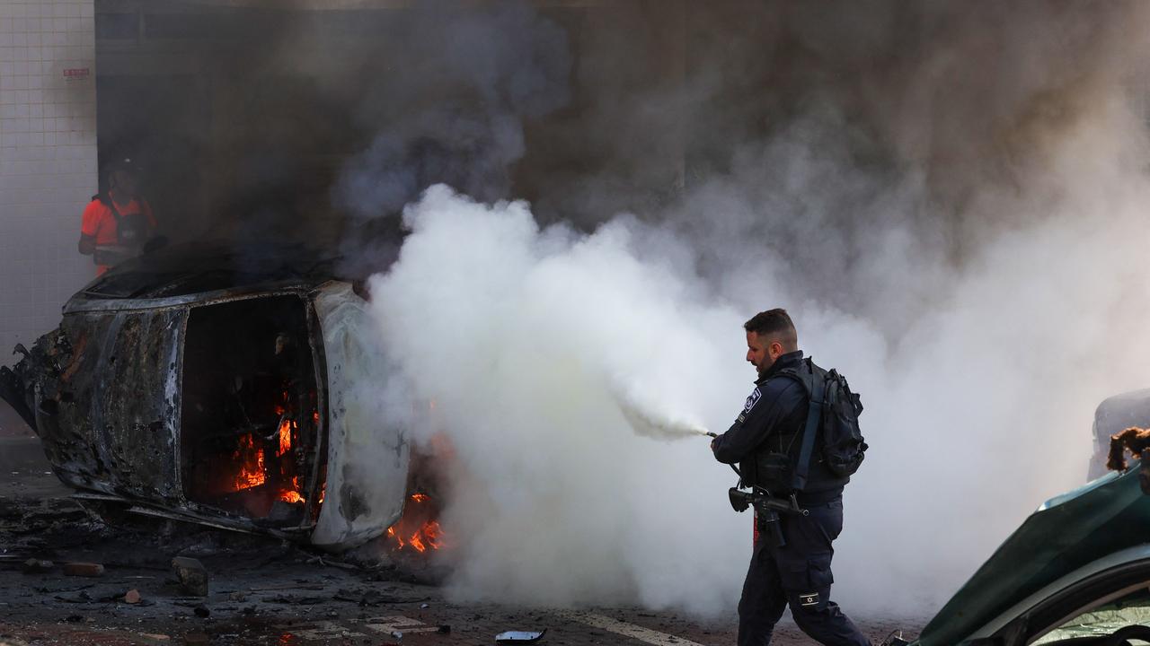 A member of Israeli security forces tries to extinguish fire on cars following a rocket attack from the Gaza Strip. Picture: AFP