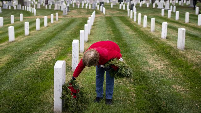 ARLINGTON, VA - DECEMBER 18: A woman places a wreath on a tombstone at Arlington National Cemetery, on December 18, 2021 in Arlington, Virginia. The 30th annual Wreaths Across America project places wreaths on the more than 250,000 tombstones of military servicemen and women at Arlington National Cemetery.   Al Drago/Getty Images/AFP == FOR NEWSPAPERS, INTERNET, TELCOS & TELEVISION USE ONLY ==