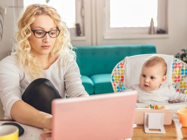 Mother wearing eyeglasses working at home office on laptop and taking care of her baby