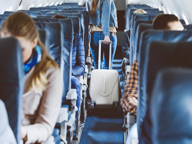 ESCAPE:  Interior of airplane with people sitting on seats. Passengers with suitcase in aisle looking for seat during flight.  Picture: Istock