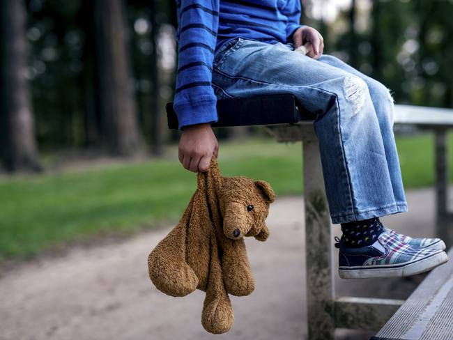 Young boy holding teddybear while alone on the bleachers