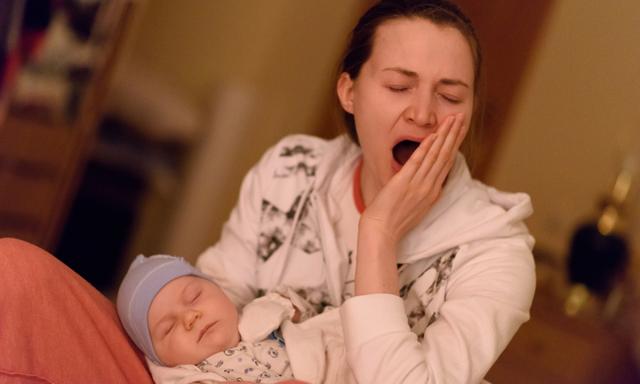 mother is yawning, holding sleeping baby in her arms