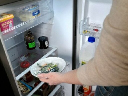 Clare takes leftover vegetables from her bare fridge.