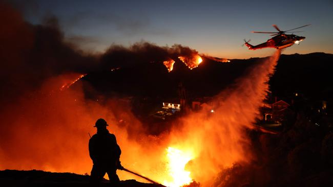 Fire personnel respond to homes destroyed while a helicopter drops water as the Palisades Fire grows in Pacific Palisades. Picture: AFP