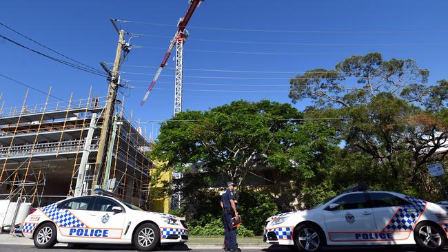 Police guard the entrance to an apartment complex, behind trees, where the body of a 49 year-old woman was found in Toowong. Pic: AAP Image/Dan Peled