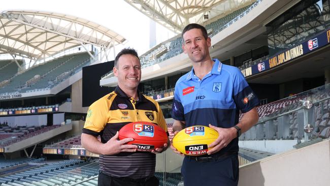 Glenelg coach Darren Reeves (left) and Sturt coach Martin Mattner eye off the Thomas Seymour Hill premiership cup which is up for grabs at Sunday’s SANFL grand final. Picture: David Mariuz/SANFL