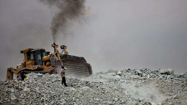 A bulldozer moves rubble as a villager searches for tiny flecks of gold at Barrick Gold’'s North Mara mine in 2010.