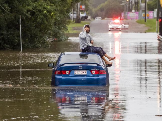 A man sits on his car roof after the vehicle became stuck in floodwaters in Carina in Brisbane. Picture: Richard Walker