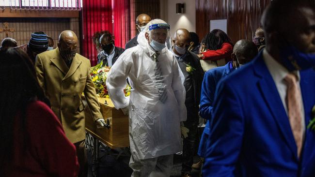 An undertaker, wearing a protective suit and a face shield, and relatives escort the coffin containing the remains of a COVID-19 victim during a funeral in Johannesburg. Picture: AFP