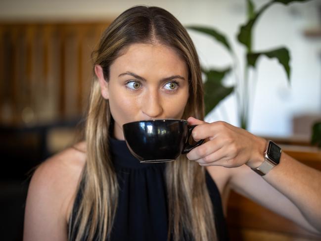 Young female in a cafe or restaurant dining inside and holding a coffee mug. Sipping or smelling caffeinated drink. Morning routine happiness in the daylight.
